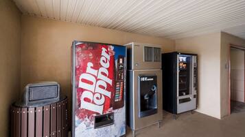 Een rij automaten, waaronder een Dr Pepper automaat, in een gang met een beige plafond en muren.
