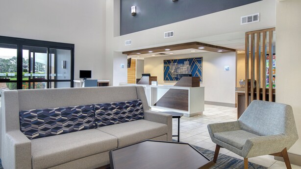 A modern lobby with a sofa, armchair, and a coffee table. There is a reception desk and a vending machine in the background. - Holiday Inn Express Marietta - Atlanta Northwest by IHG (Marietta)