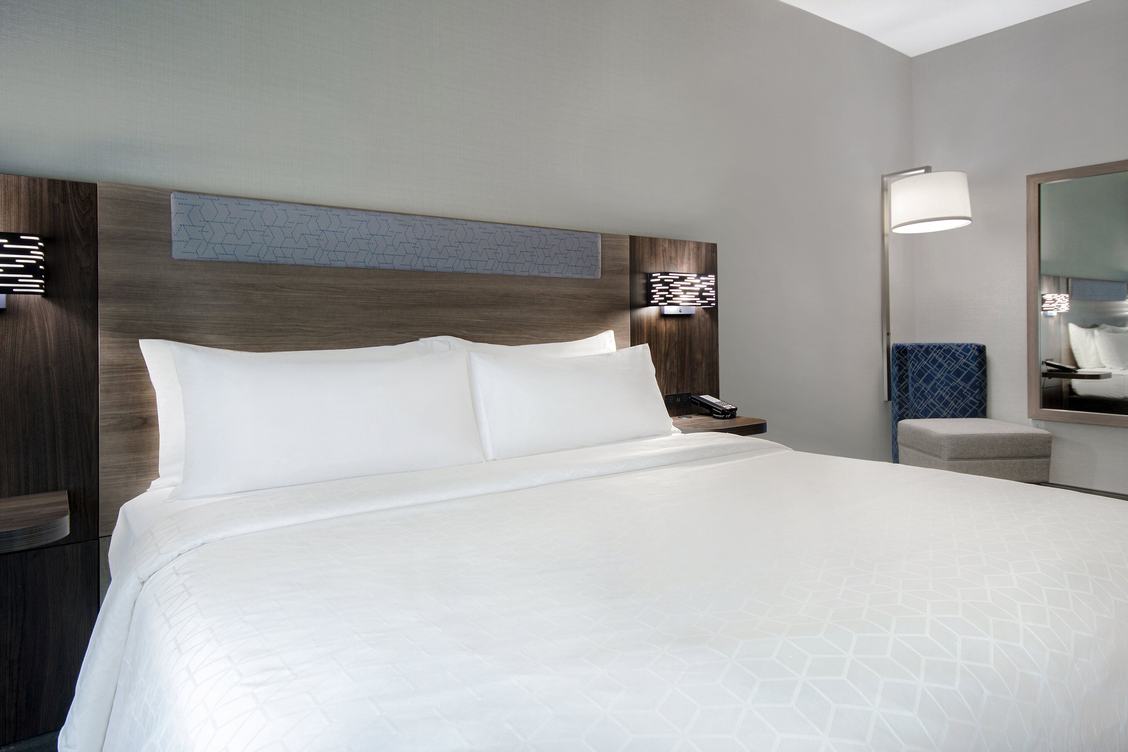 Une chambre d’hôtel avec un grand lit, une table de chevet, une lampe de chevet, un miroir et un luminaire fixé au mur.