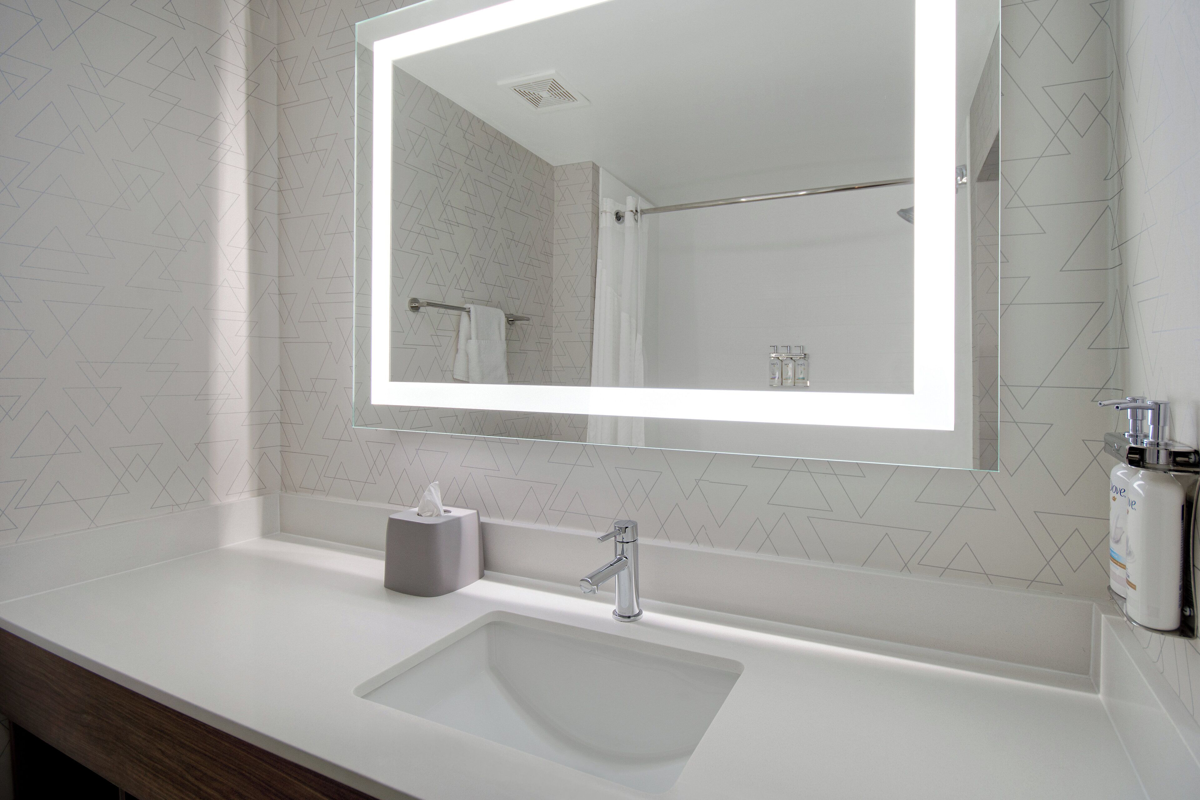 Une salle de bain moderne avec un grand miroir, un lavabo et un espace douche.