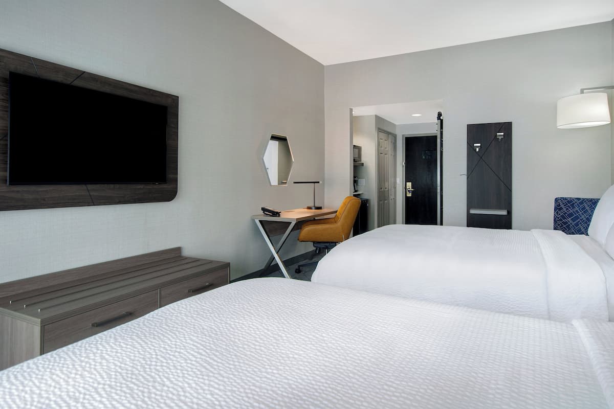 Una habitación de hotel con dos camas, un escritorio, una silla, un televisor y un espejo.