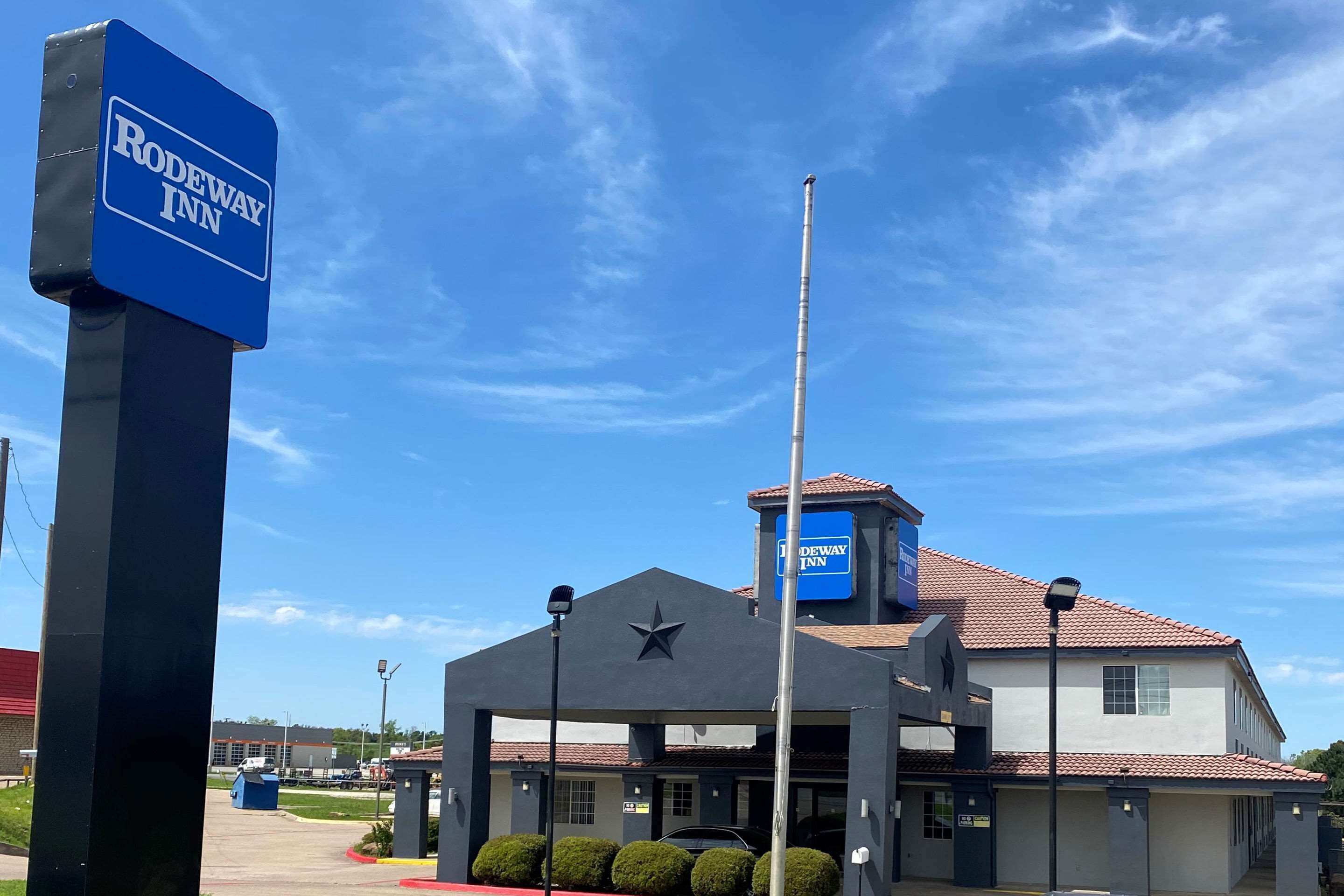A Rodeway Inn building with a star logo, a blue sign, and a clear blue sky.