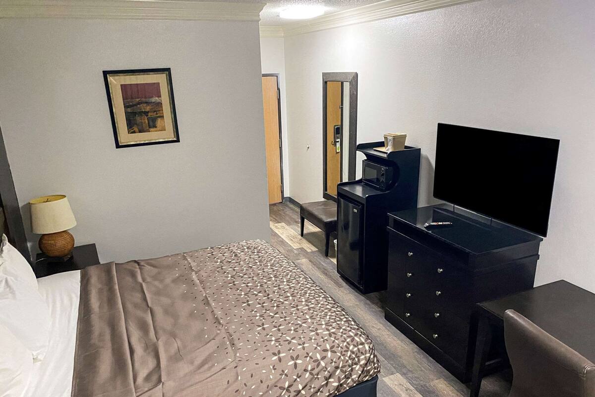 Habitación de hotel con cama, escritorio con computadora, televisor y puerta que da a otra habitación.