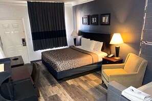 Una habitación de hotel con una cama, dos mesitas de noche, un escritorio, una silla, una lámpara y una puerta.