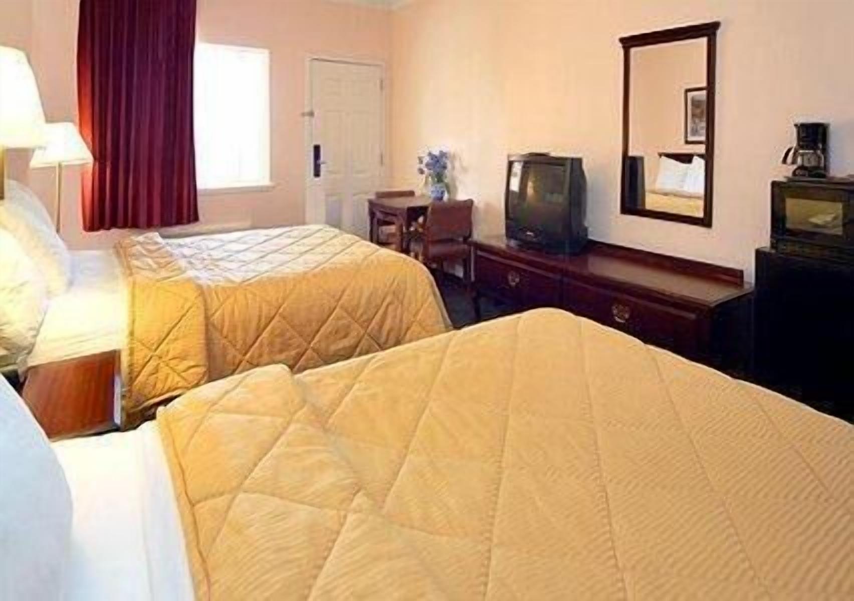 A hotel room with two beds, a television, a desk, and a chair.