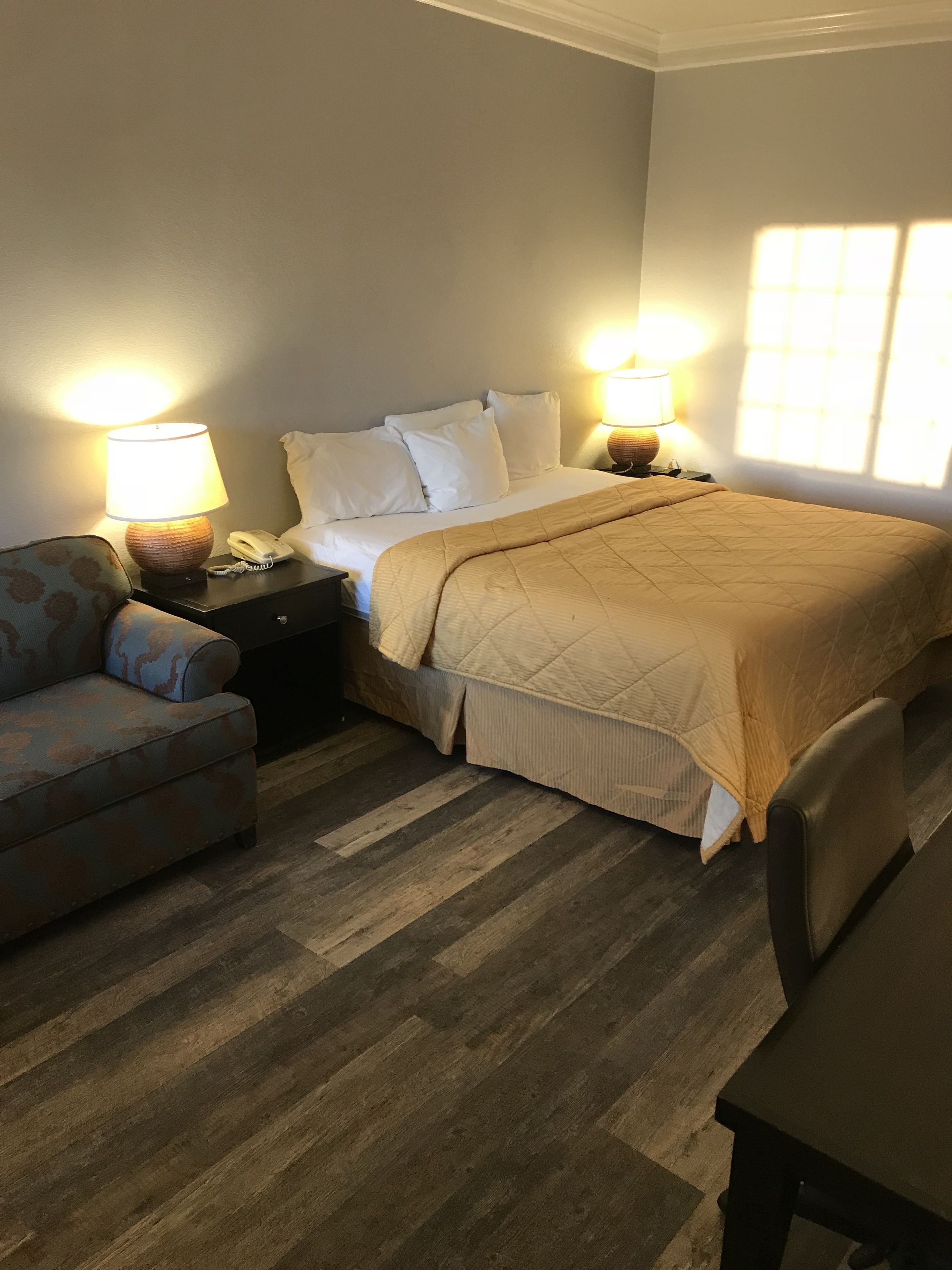 Un dormitorio ordenado con cama, lámparas de noche, una mesita de noche, una silla y una pequeña mesa.
