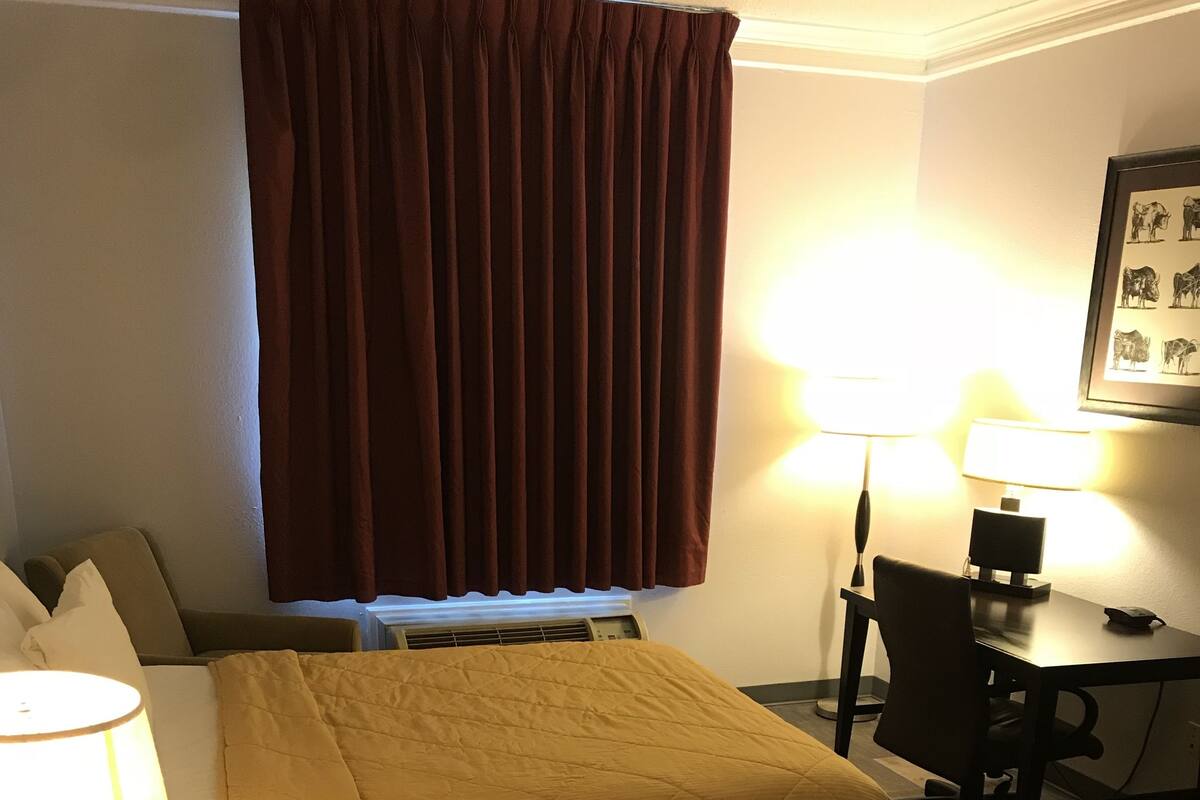 Habitación de hotel con dos camas, un escritorio, una silla, una lámpara y un cuadro en la pared.