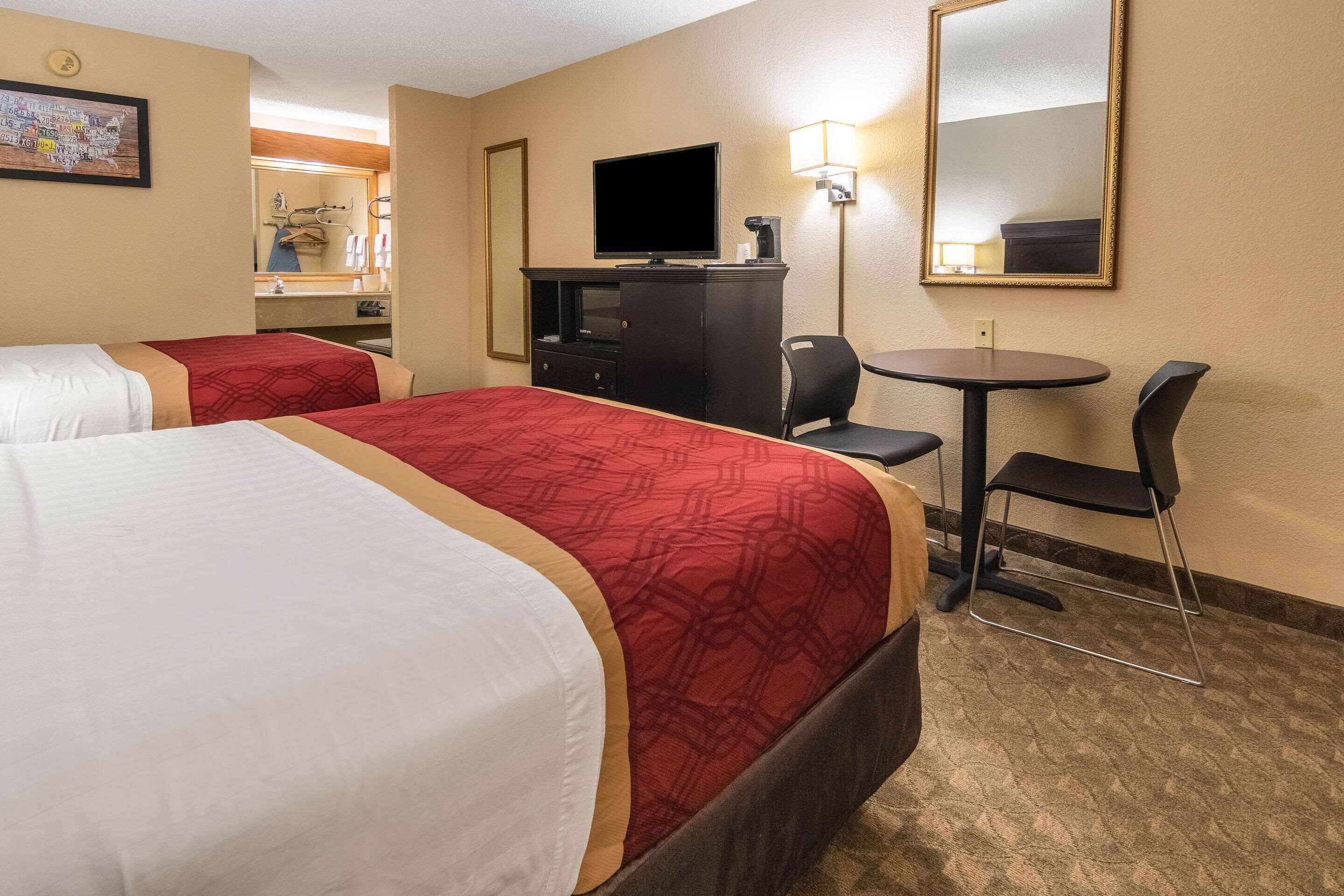 A hotel room with two beds, a desk, a chair, a television, and a mirror.