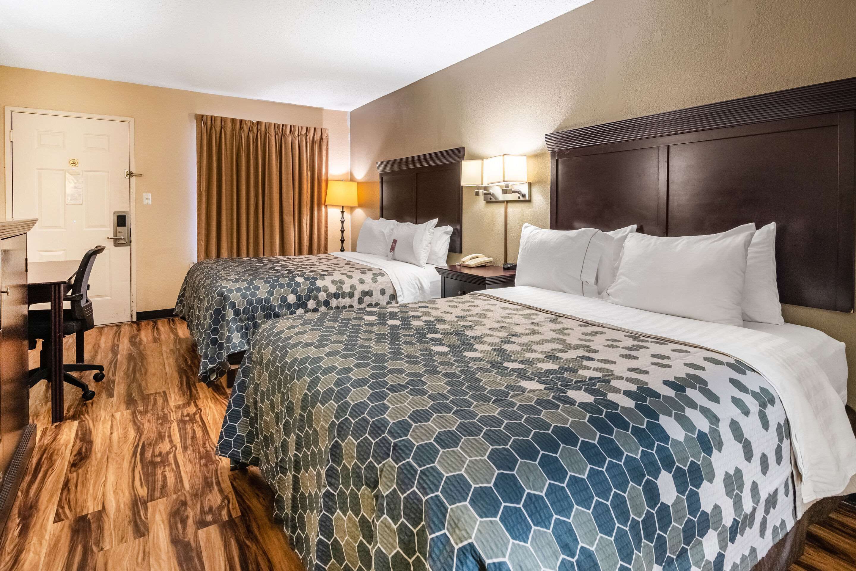 A hotel room with two beds, a desk, a chair, and a door.