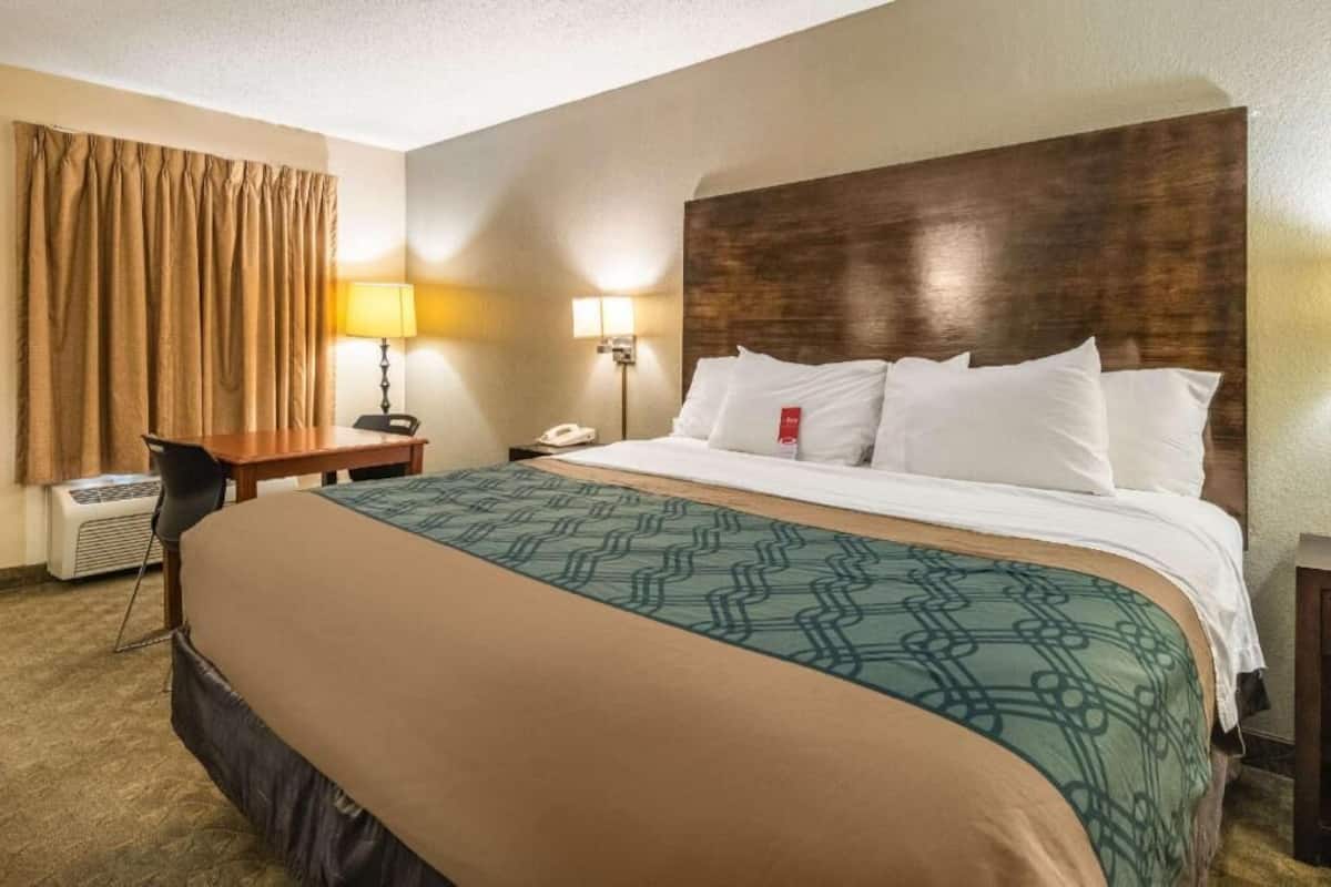 A hotel room with a bed, a desk, a lamp, a phone, and a window with curtains.