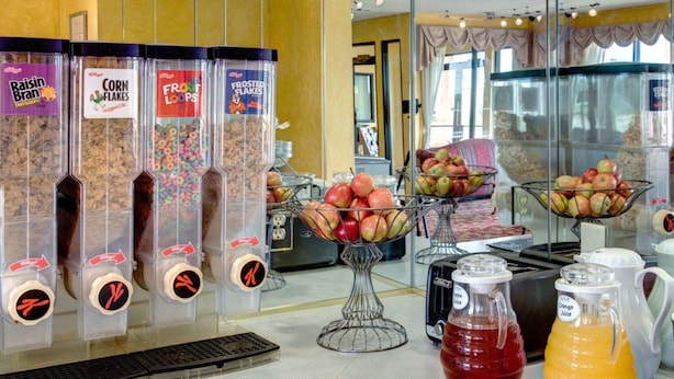 Un área de desayuno con dispensadores de cereales, cuencos de fruta y jarras de jugo.
