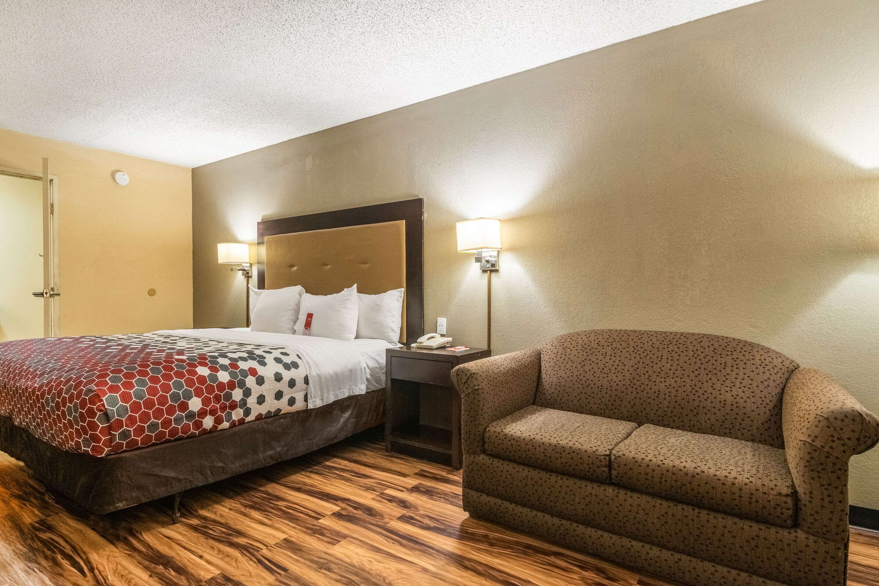 Una habitación de hotel con cama, mesita de noche, lámpara y un sillón estampado.