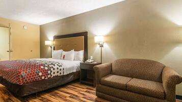 Una habitación de hotel con cama, mesita de noche, lámpara y un sillón estampado.