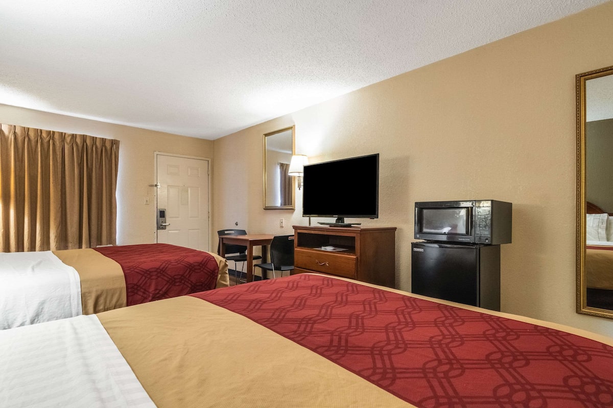 A hotel room with two beds, a desk with a chair, a television, a microwave, and a mirror on the wall.