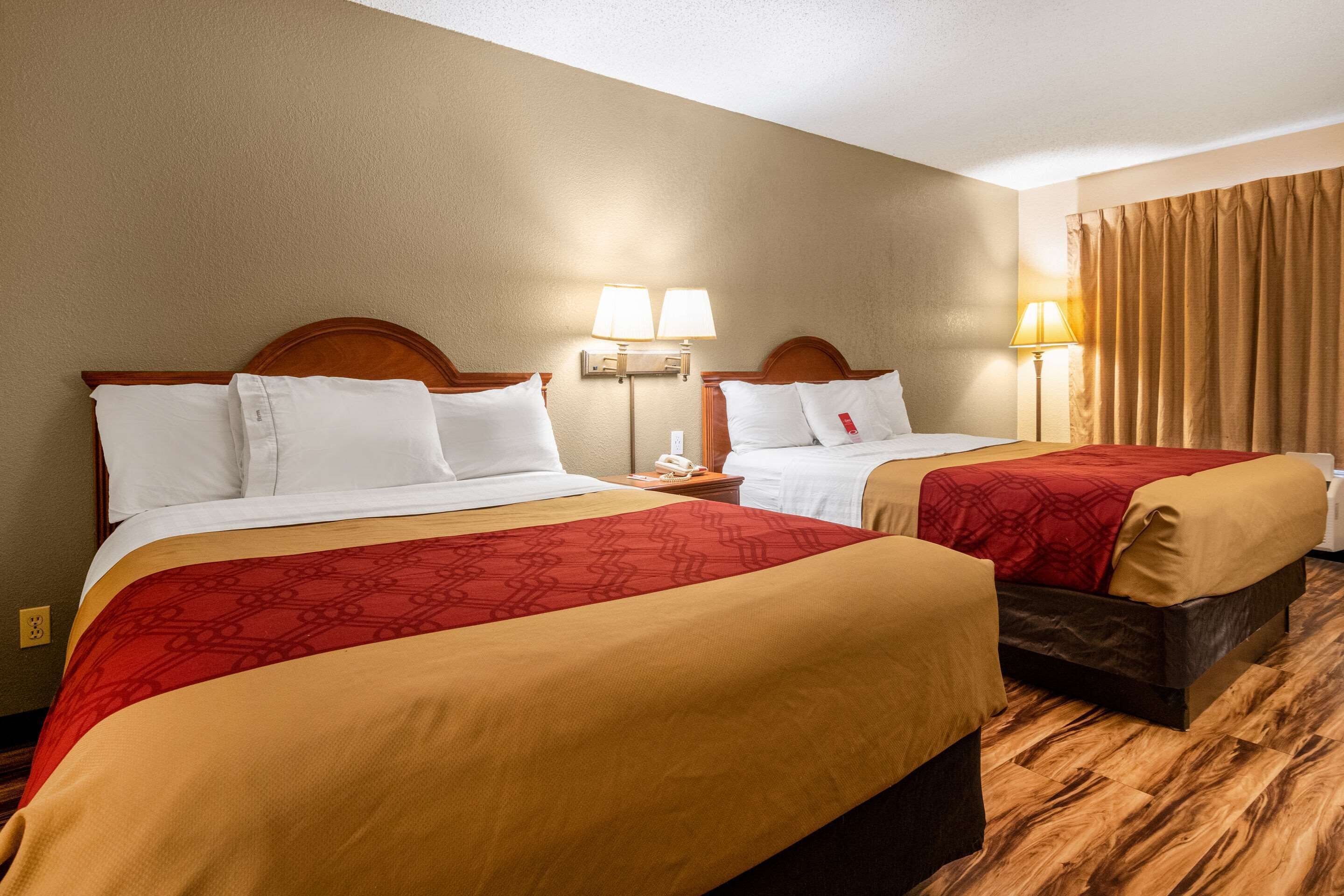 Une chambre d’hôtel avec deux lits, chacun recouvert d’une courtepointe rouge et beige, dotée d’une tête de lit en bois, de lampes de chevet et d’un téléphone sur la table de chevet.