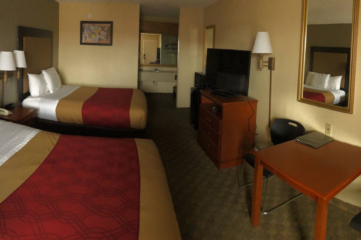 A hotel room with two beds, a desk, a chair, a dresser, a TV, and a mirror.