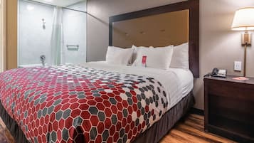 Habitación de hotel con cama, mesita de noche con lámpara, zona de ducha y teléfono instalado en la pared.