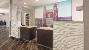 A reception area with a modern design, featuring a reception desk, a wall-mounted information board, and a decorative mural of a building. - La Quinta Inn & Suites by Wyndham Oklahoma City Norman (Norman)