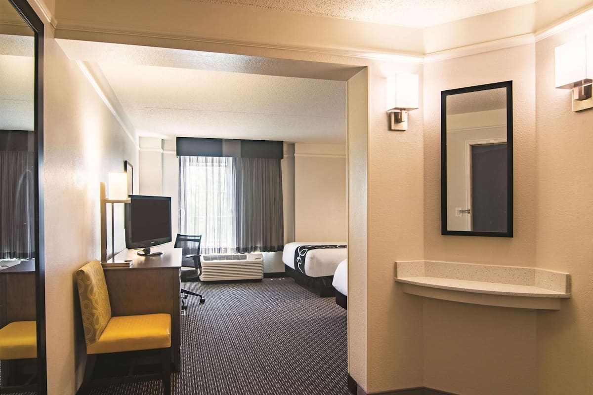 A hotel room with a desk, chair, bed, and a large mirror.