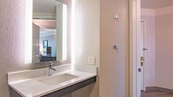 A modern bathroom with a large mirror, a sink, and a door leading to another room.