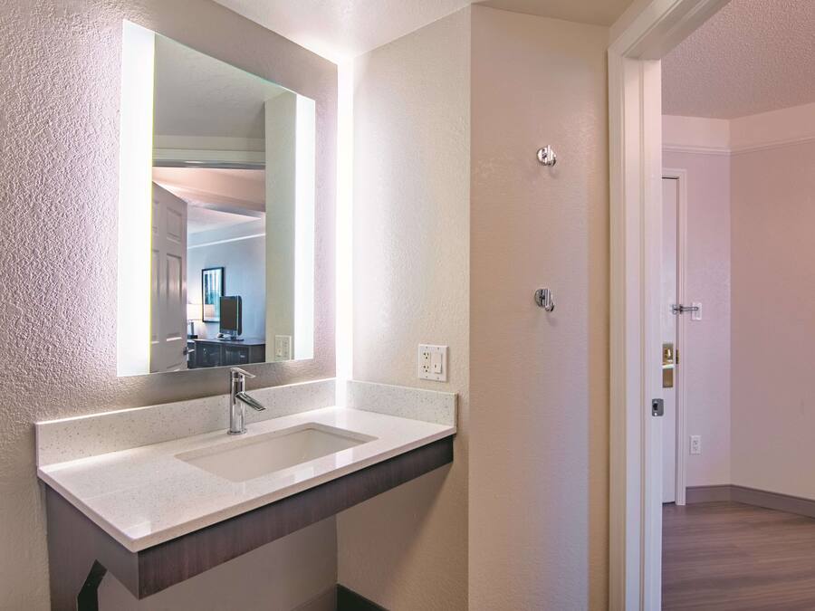 A modern bathroom with a large mirror, a sink, and a door leading to another room.