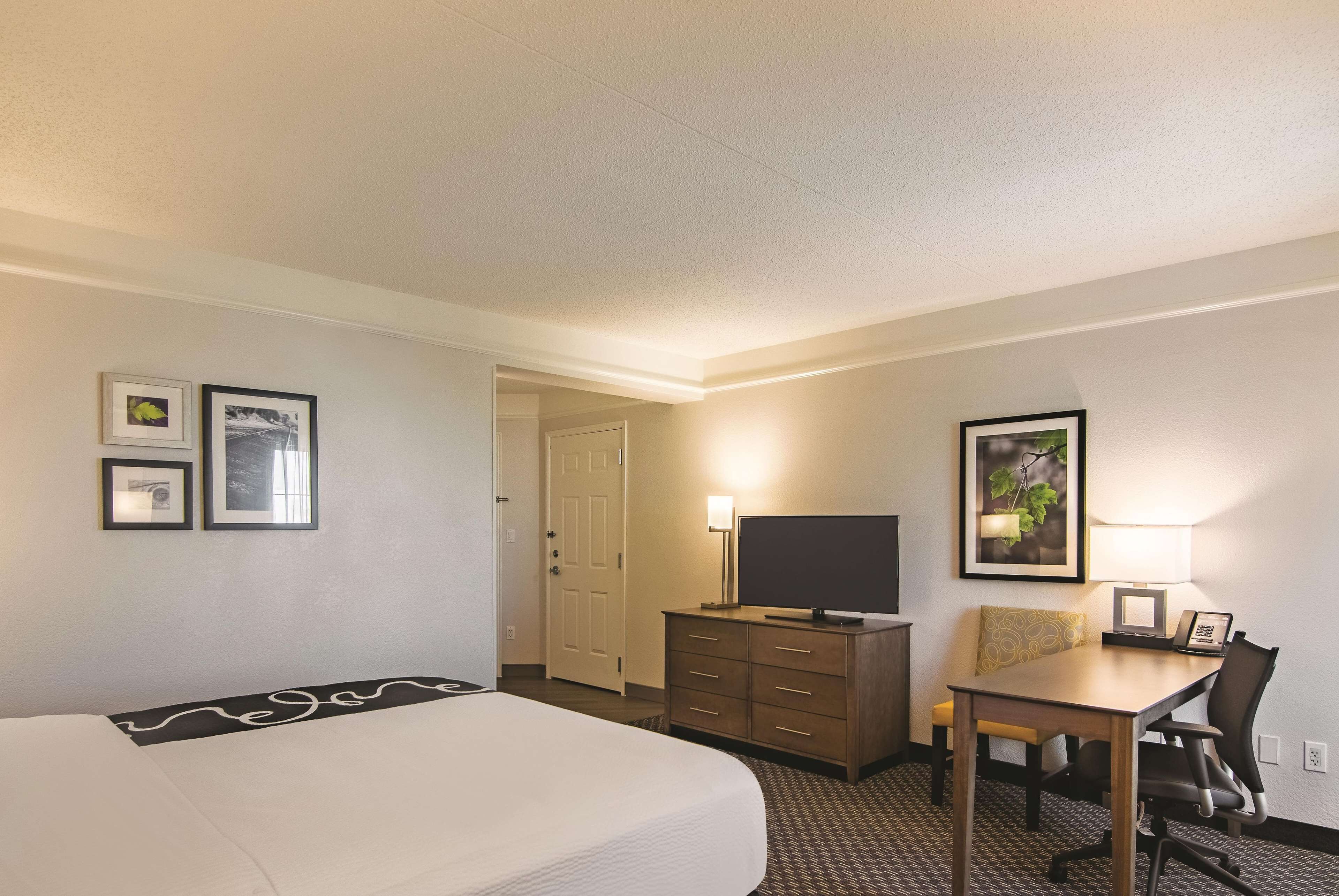 Une chambre d’hôtel avec un lit, un bureau et une chaise, une télévision et une porte.