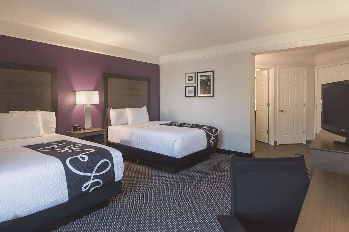 A hotel room with two beds, a TV, a desk, and a door.
