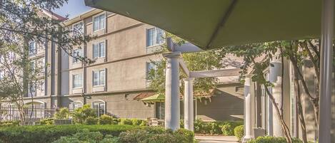 Un edificio de varios pisos con un espacio exterior techado, columnas y un banco.