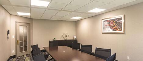 A conference room with a long table, six chairs, a door, a clock, and a framed picture on the wall.