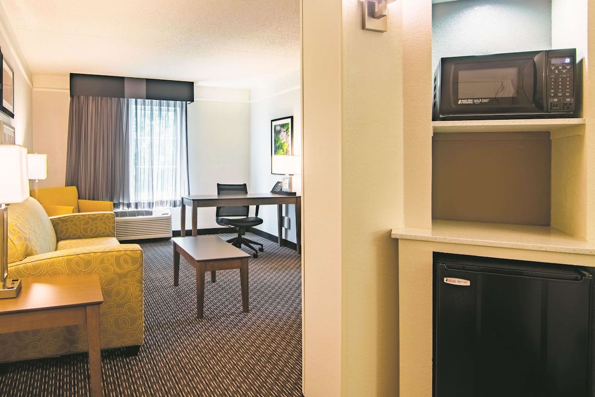 A hotel room with a yellow sofa, a small table, a desk with a chair, a microwave, and a mini fridge.