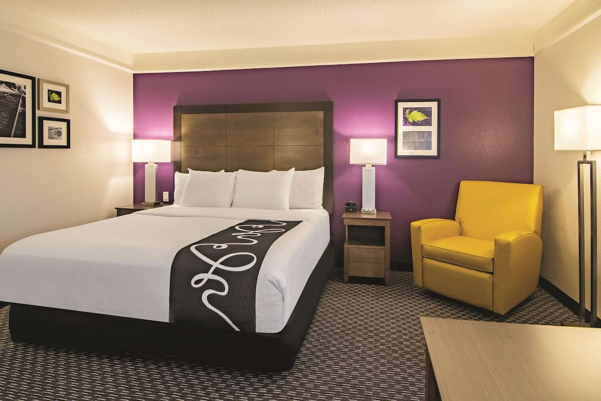 A hotel room with a large bed, two bedside tables with lamps, a small table, a yellow armchair, and a floor lamp.