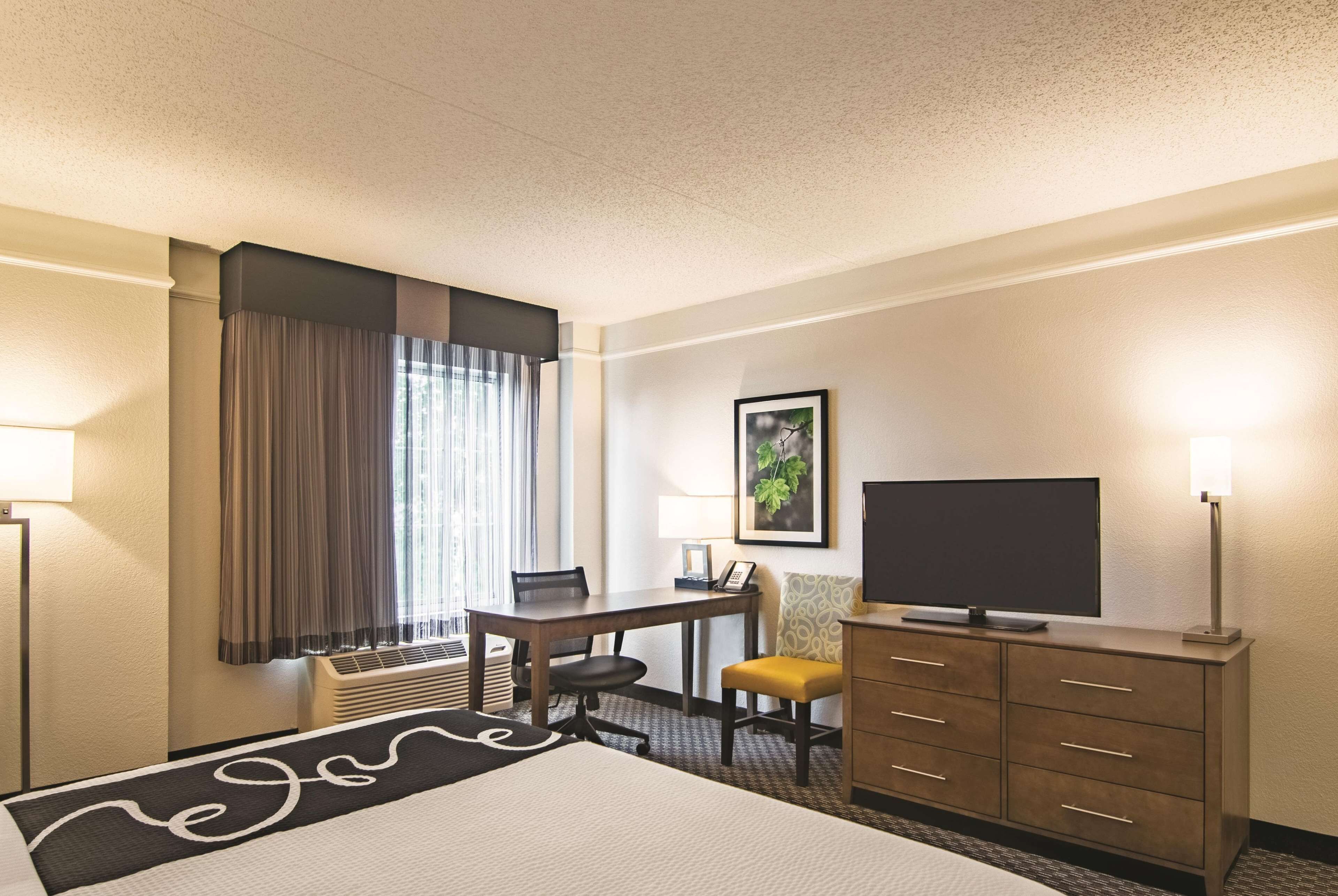 A hotel room with a bed, a desk, a chair, a television, and a dresser.