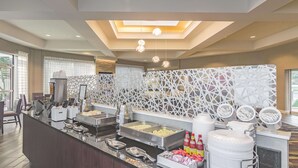 A hotel breakfast area with a buffet setup, including various food items and a coffee station. - La Quinta Inn & Suites by Wyndham Oklahoma City Norman (Norman)