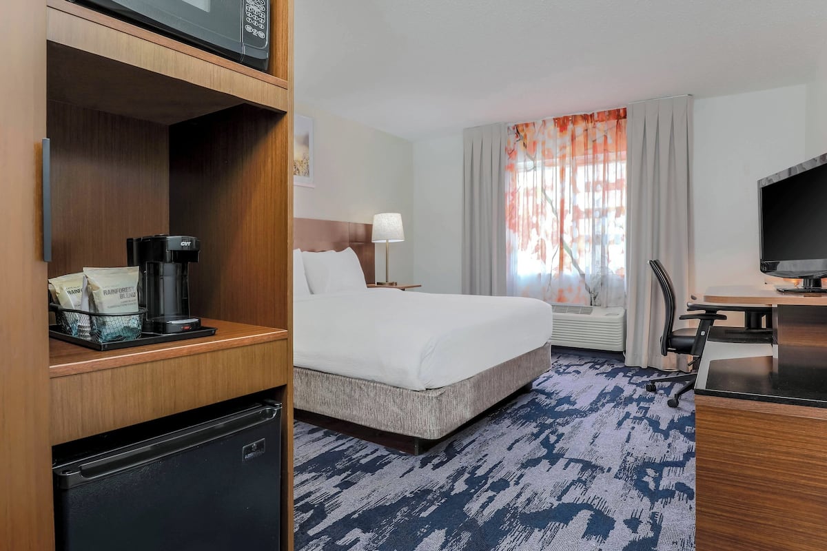 A hotel room with a bed, a desk with a computer, a coffee maker, and a TV.