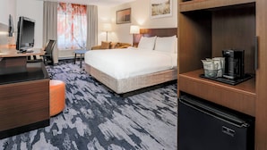 A hotel room with a bed, a desk with a TV, a coffee machine, and a refrigerator.