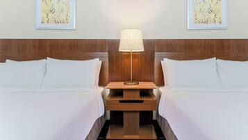 Una habitación de hotel con dos camas, una mesita de noche con lámpara y dos cuadros enmarcados en la pared.