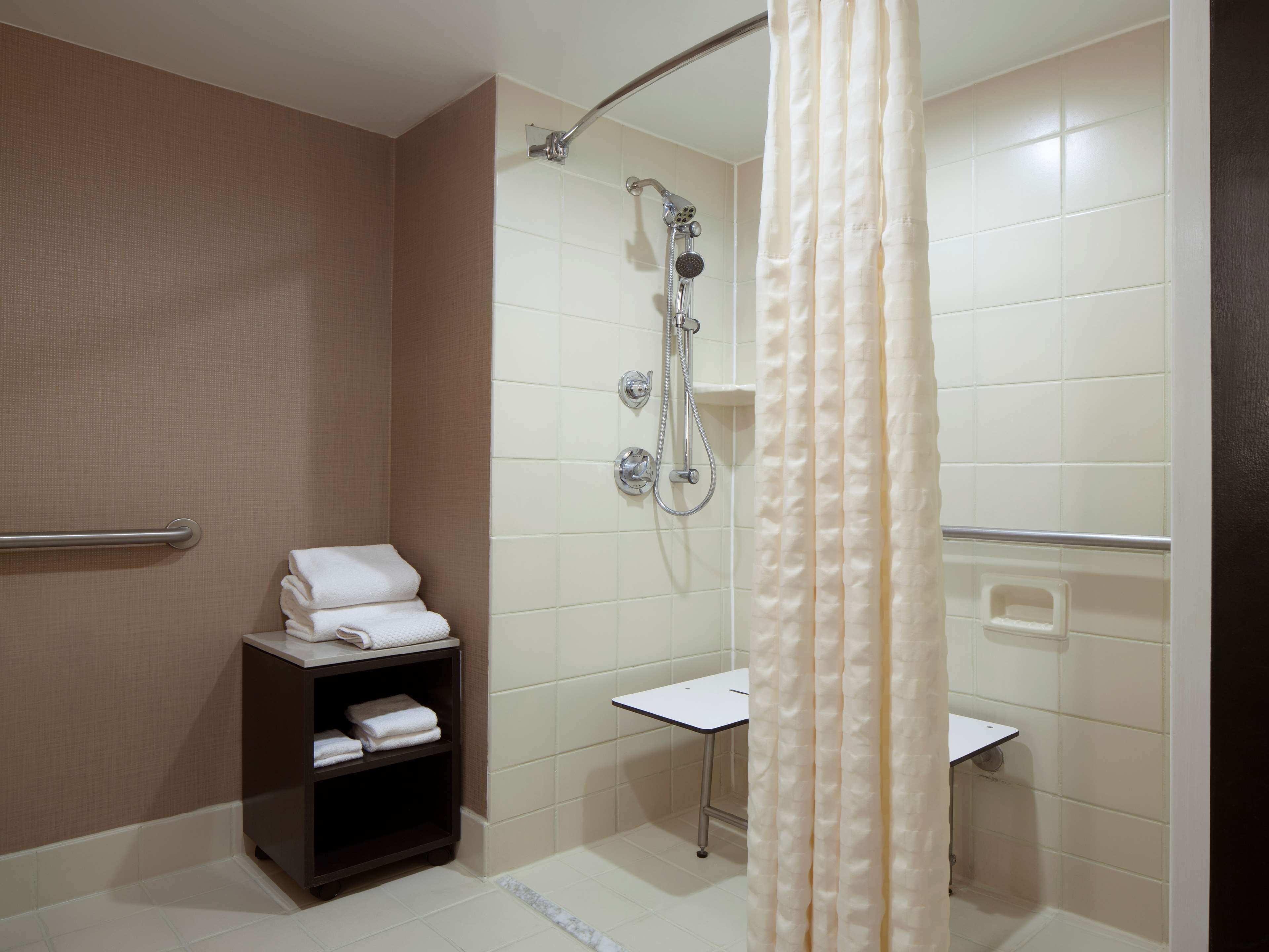 Een badkamer met een douche, toilet en wastafel. Handdoekrek met gevouwen handdoeken en een plank met meer handdoeken.