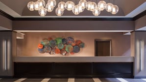 A lobby with a modern design, featuring a reception desk, a wall-mounted art installation, and a patterned floor. - Embassy Suites by Hilton Houston Near the Galleria (Houston)