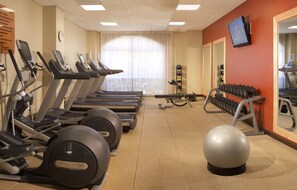 Een sportschool met loopbanden, elliptische trainers, een hometrainer en een set dumbbells.
