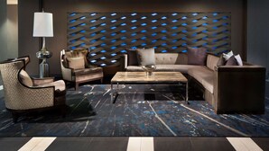 A modern living room with a sectional sofa, armchairs, a coffee table, and a patterned wall with blue lighting accents. - Embassy Suites by Hilton Houston Near the Galleria (Houston)