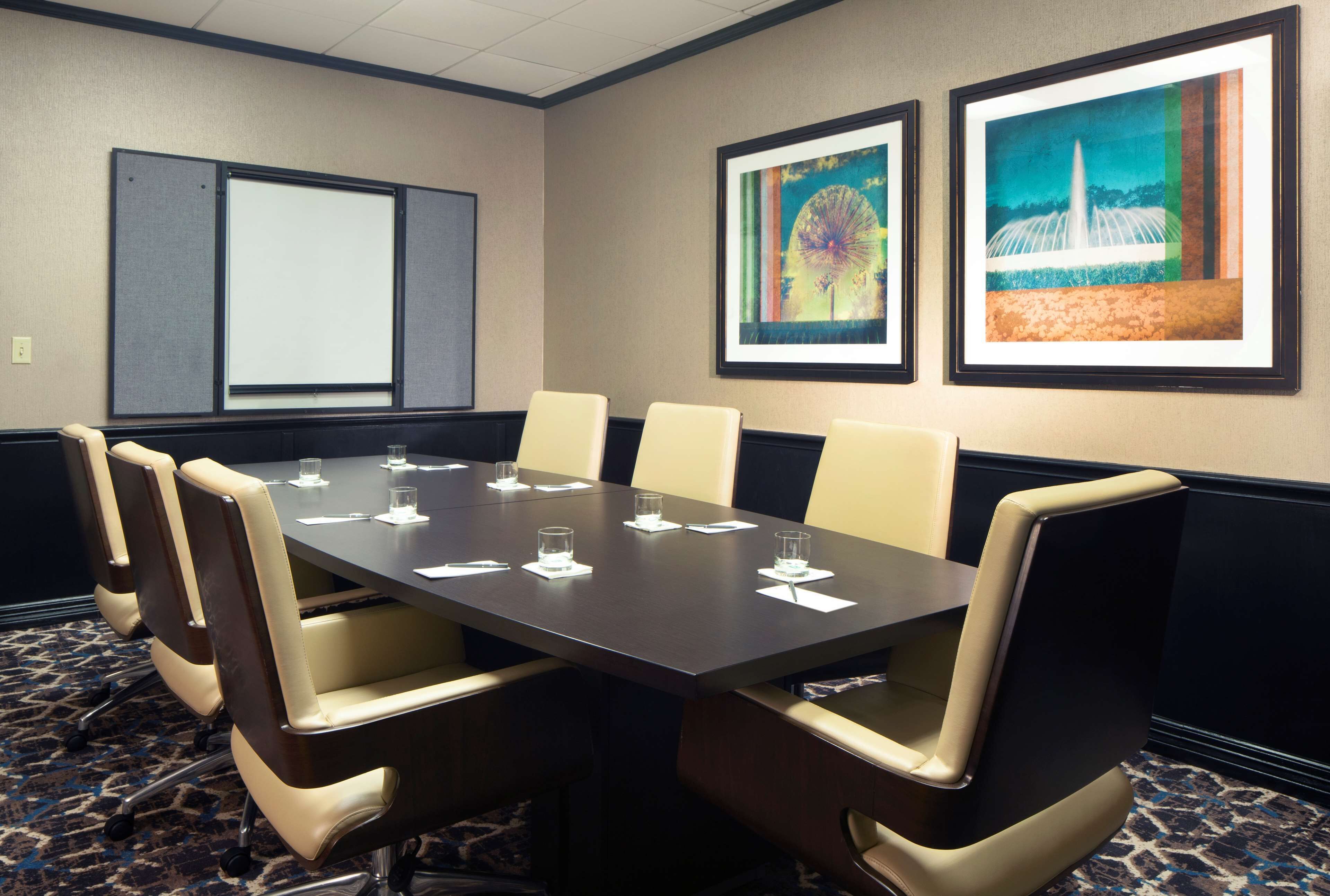 Uma sala de conferências com uma mesa comprida, seis cadeiras, uma tela de projetor e duas obras de arte emolduradas na parede.