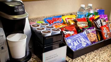 A coffee station with a Keurig coffee maker, disposable cups, and a variety of snacks and beverages.