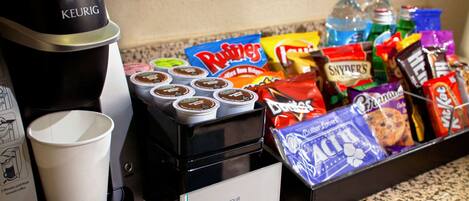 A coffee station with a Keurig coffee maker, disposable cups, and a variety of snacks and beverages.