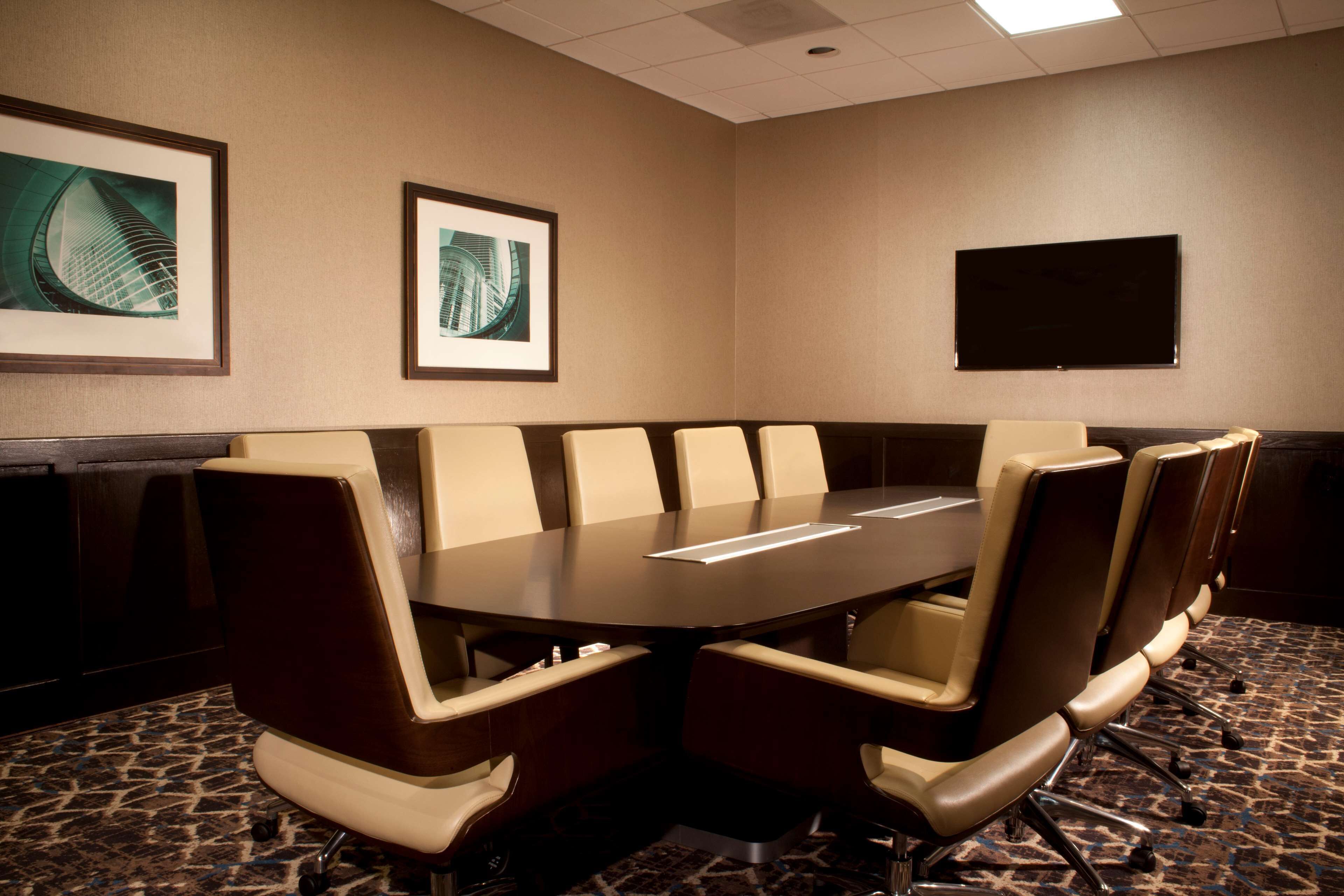 A conference room with a large table surrounded by chairs, framed artwork on the walls, and a flat-screen TV.