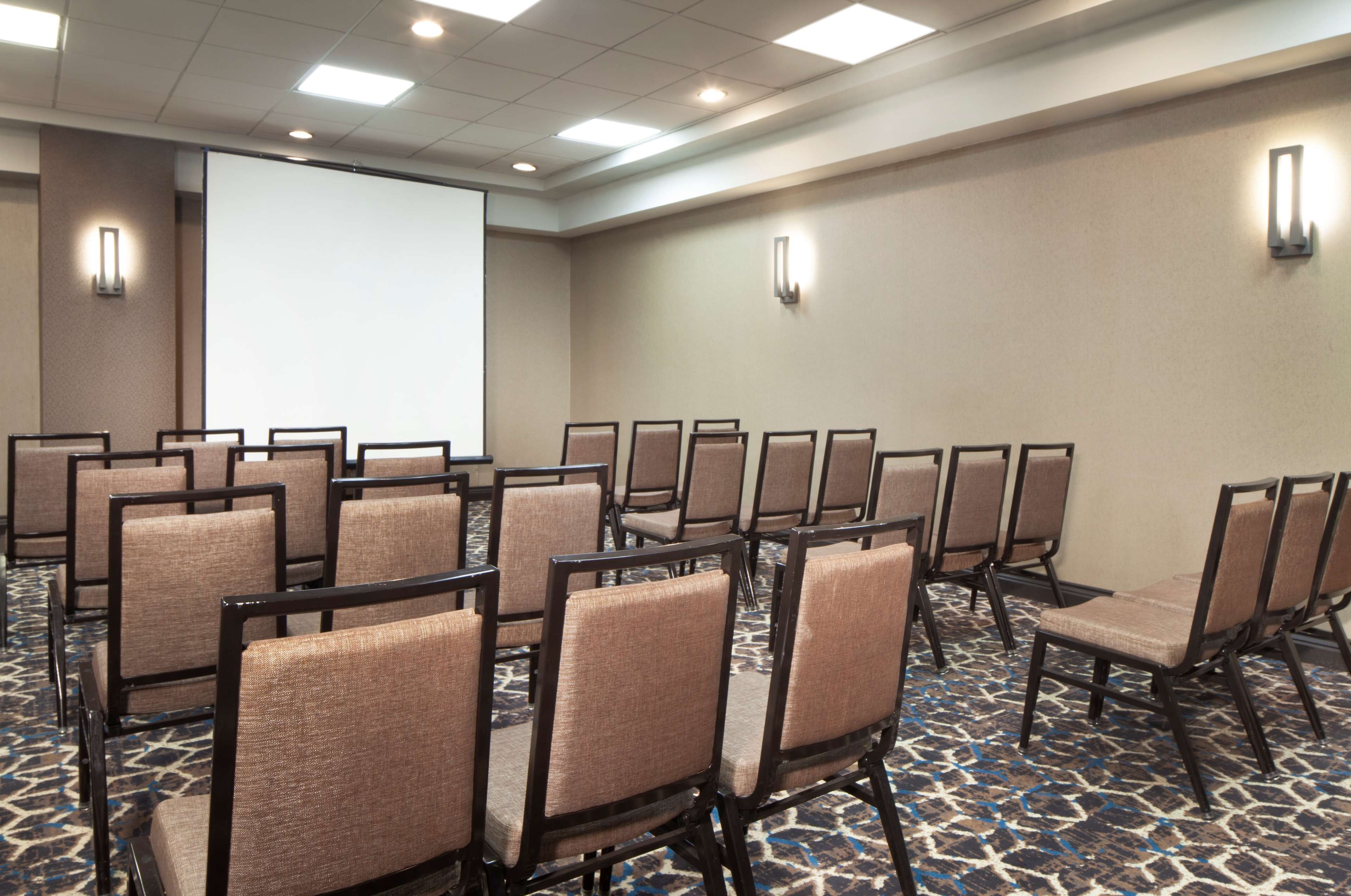 A conference room with rows of chairs, a projector screen, and a carpeted floor.