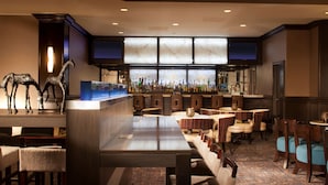 A bar area with a long counter, multiple seating options, and a decorative sculpture of a giraffe. - Embassy Suites by Hilton Houston Near the Galleria (Houston)