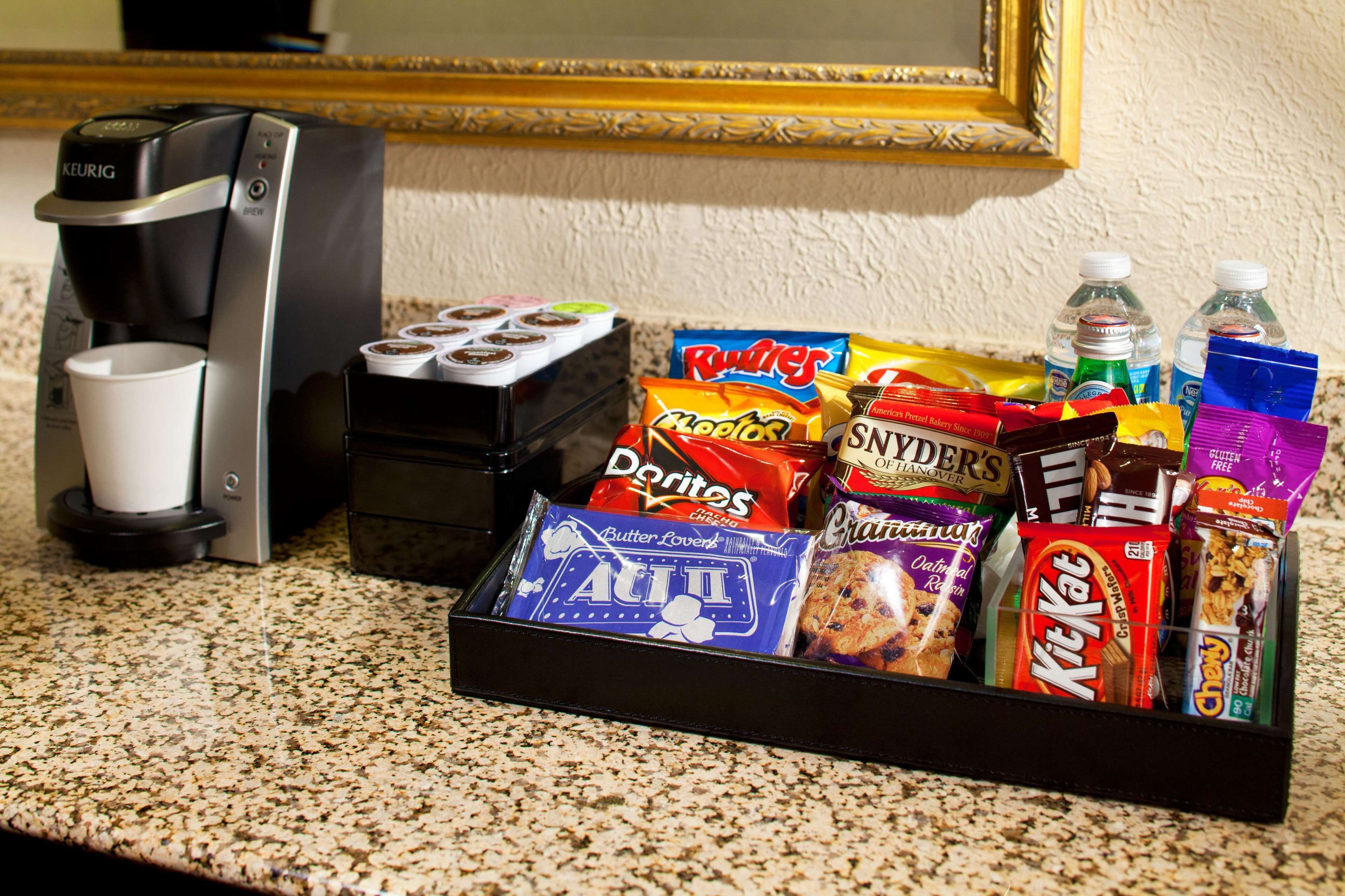 A coffee maker, a cup, and a snack tray with various items like chips, cookies, and drinks.