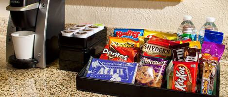 A coffee maker, a cup, and a snack tray with various items like chips, cookies, and drinks.