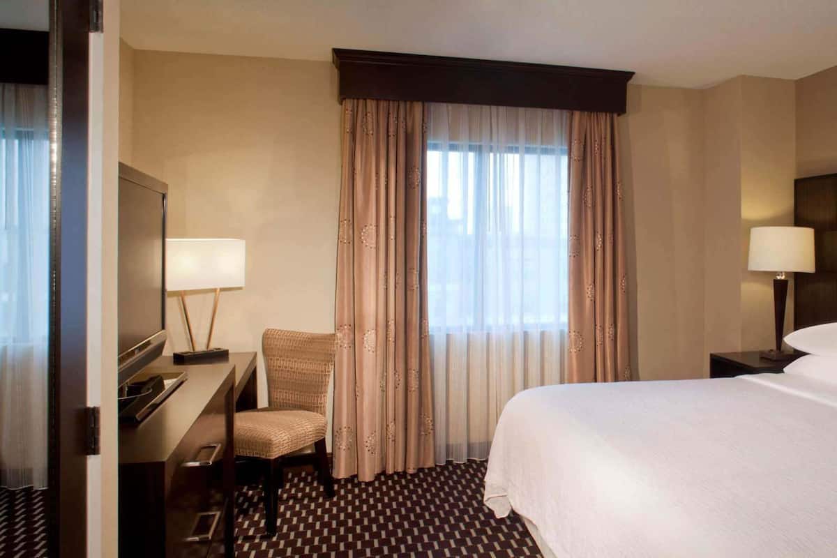 A hotel room with a bed, a desk, a chair, a TV, and curtains.