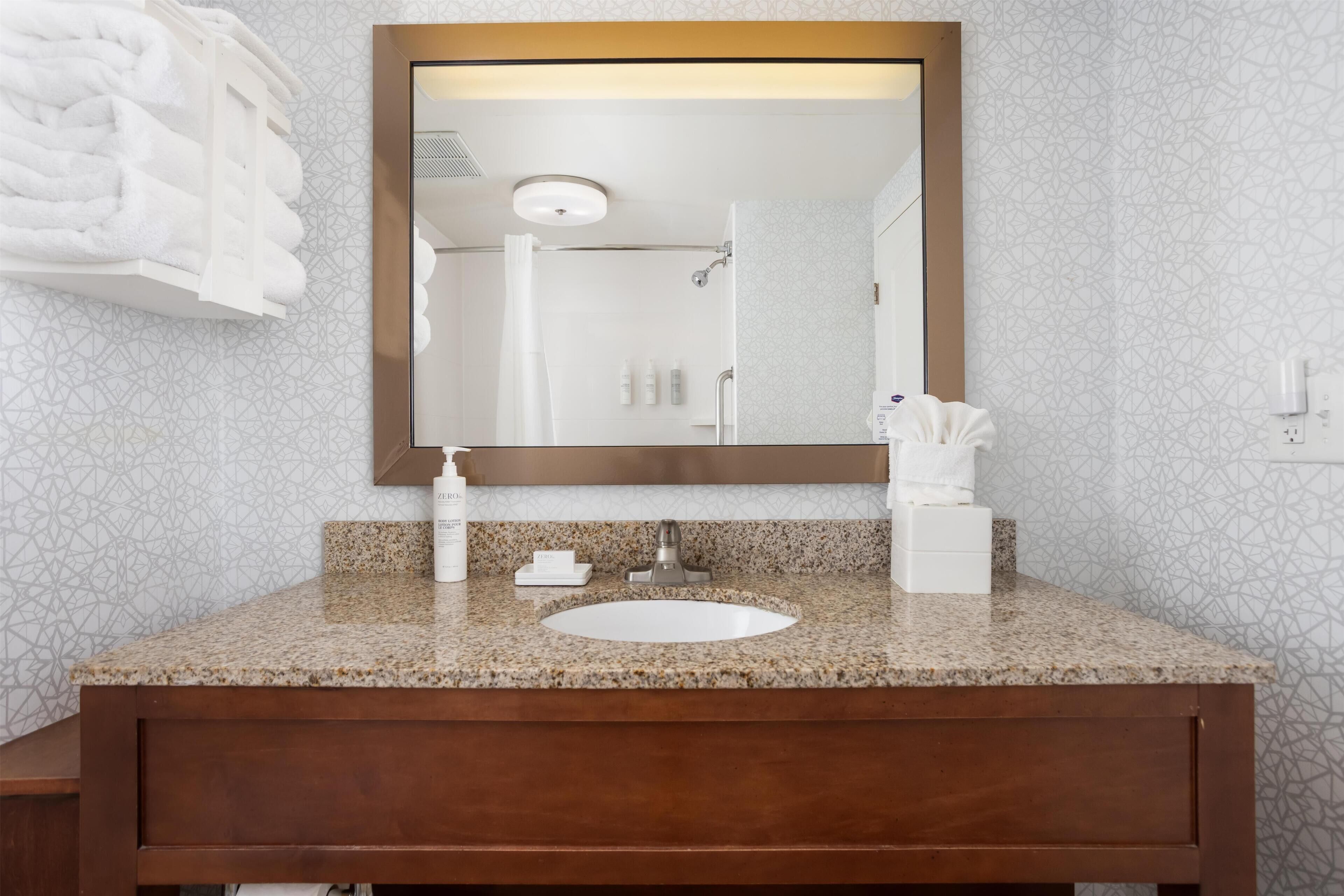 Un baño con encimera de granito, un lavabo blanco, un espejo y un perchero para toallas.